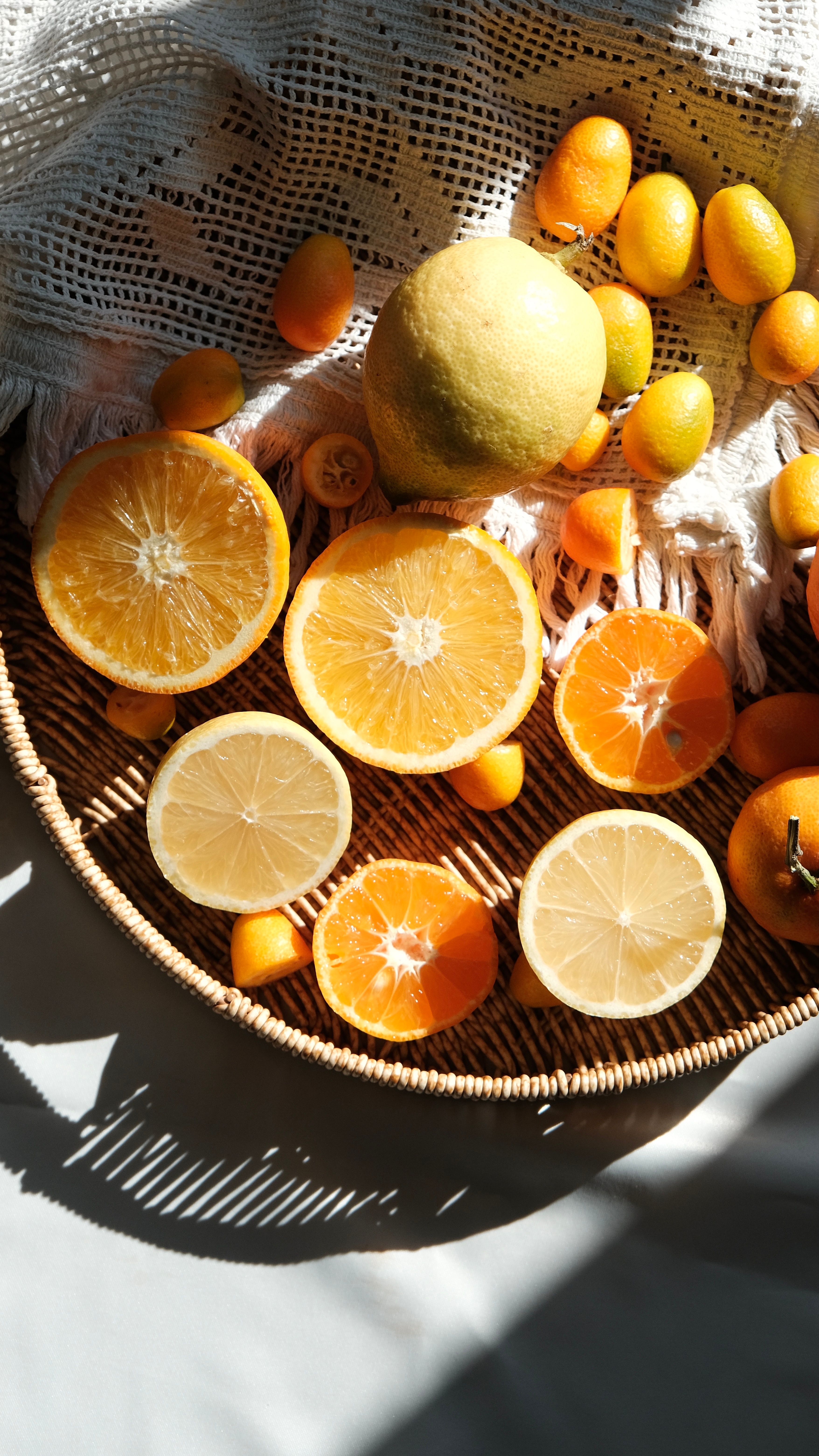A vibrant arrangement of sliced citrus fruits in sunlight on a wicker tray, evoking freshness.