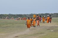 Group of pilgrims walking through a field in Anuradhapura, Sri Lanka, wearing traditional attire.
