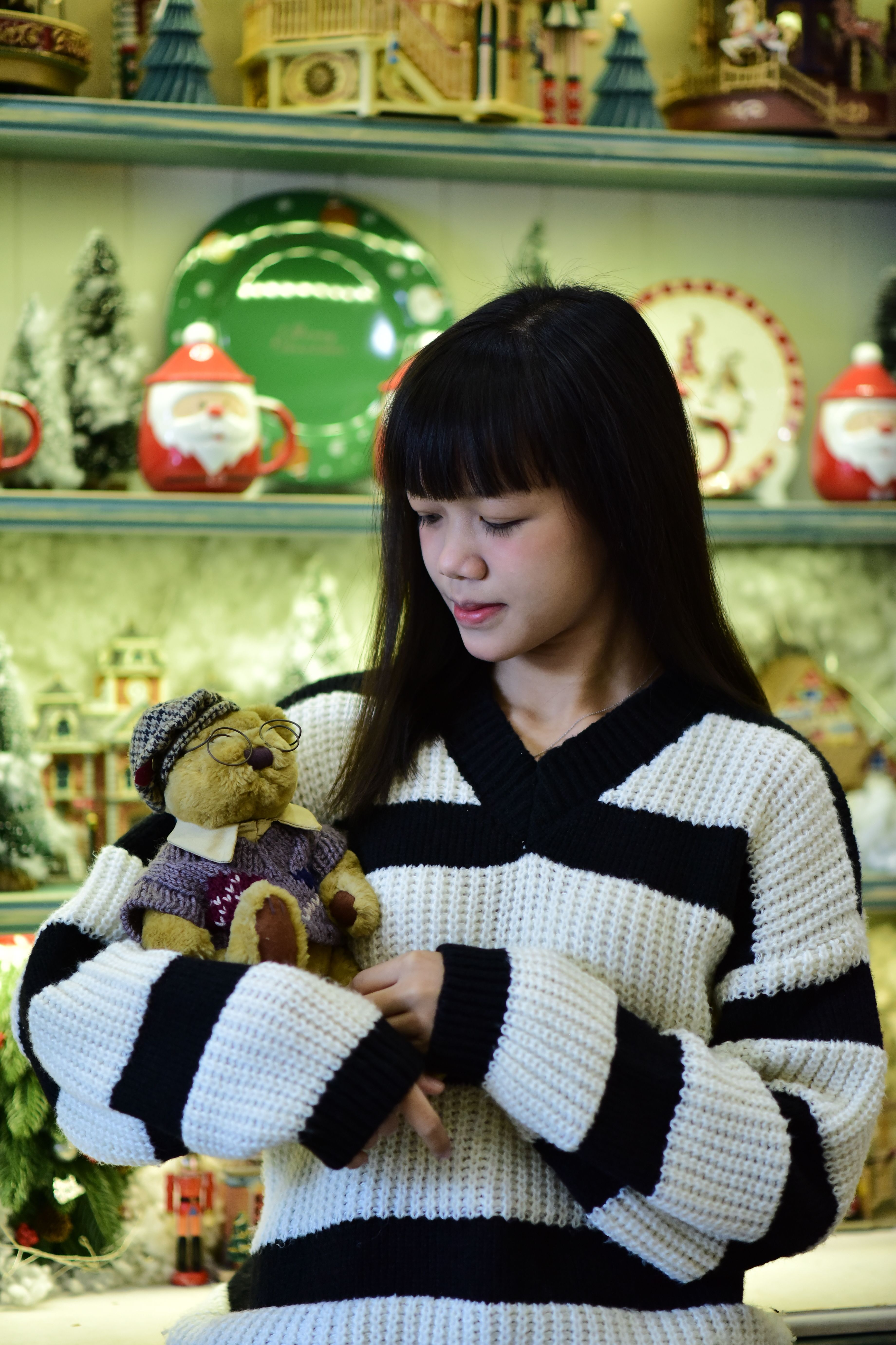 Young woman holding a teddy bear in a festive, holiday-themed shop interior.