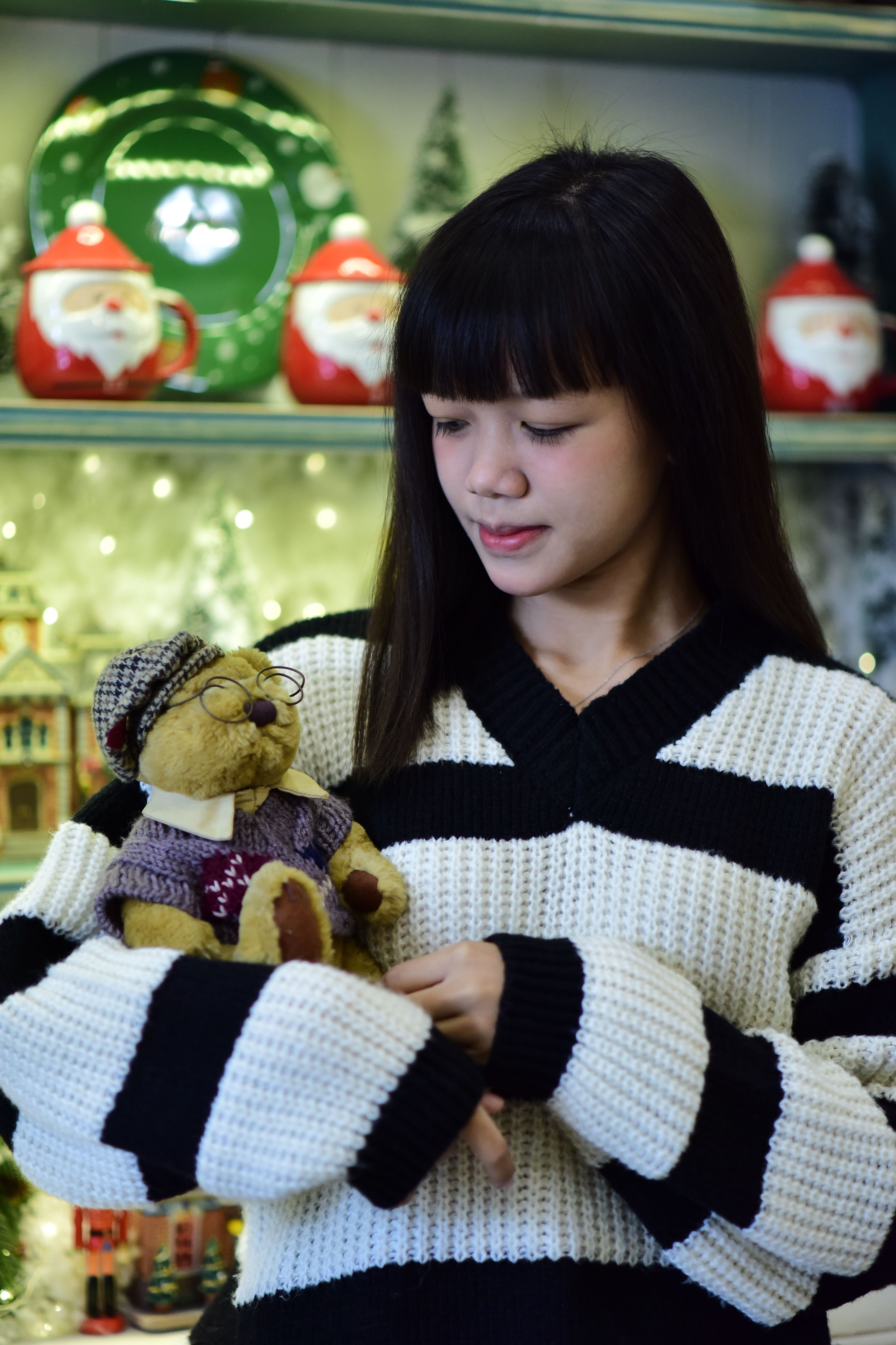 Woman in cozy sweater holding a teddy bear, surrounded by Christmas decor.