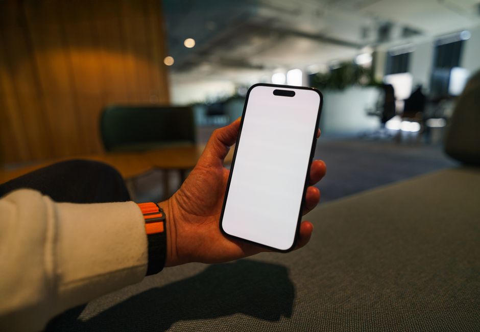 Hand in a modern office holding a smartphone with a blank screen, ready for app design mockup.