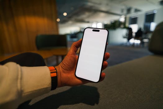 Hand in a modern office holding a smartphone with a blank screen, ready for app design mockup.