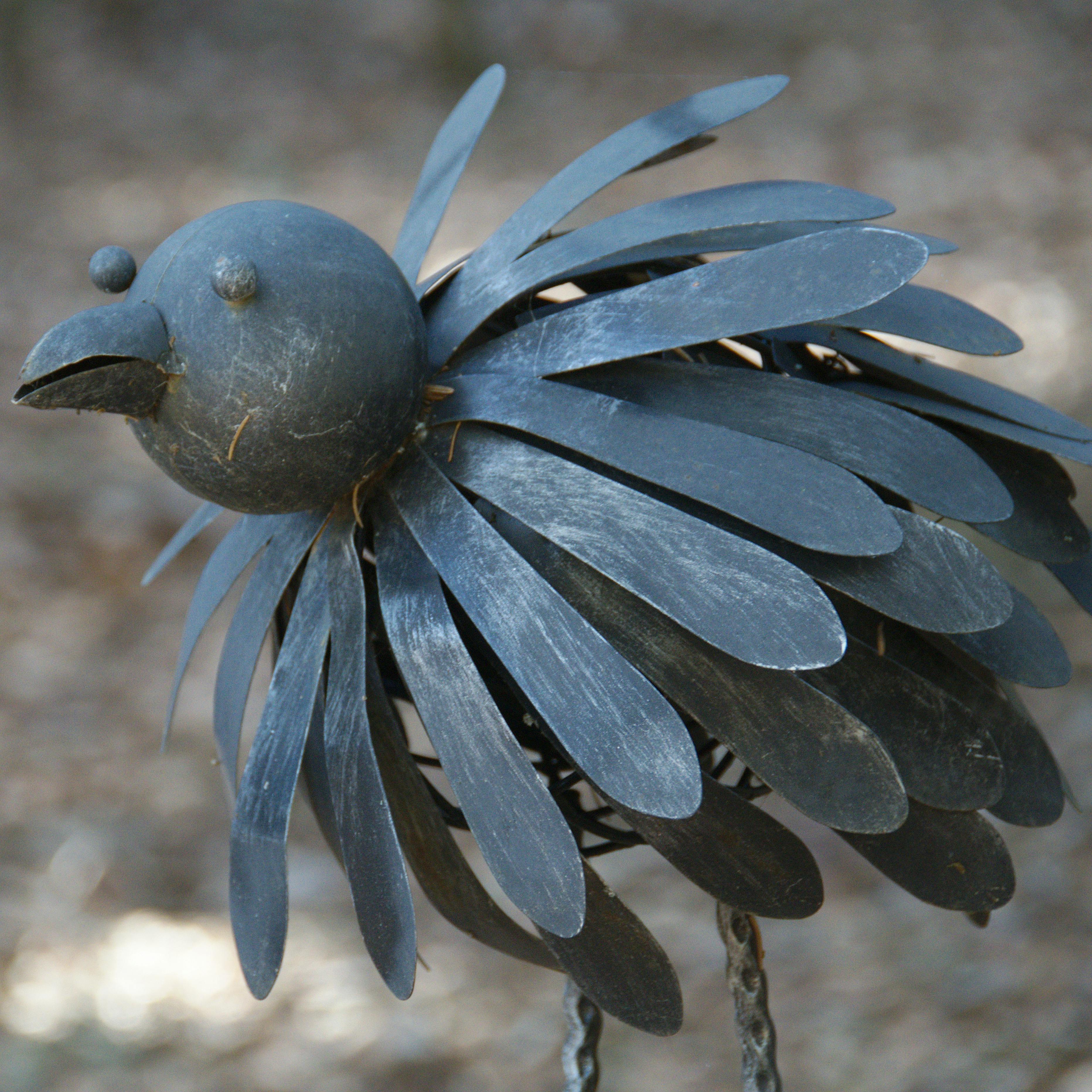 Artistic metal bird sculpture with nature background, ideal for outdoor decor inspiration.