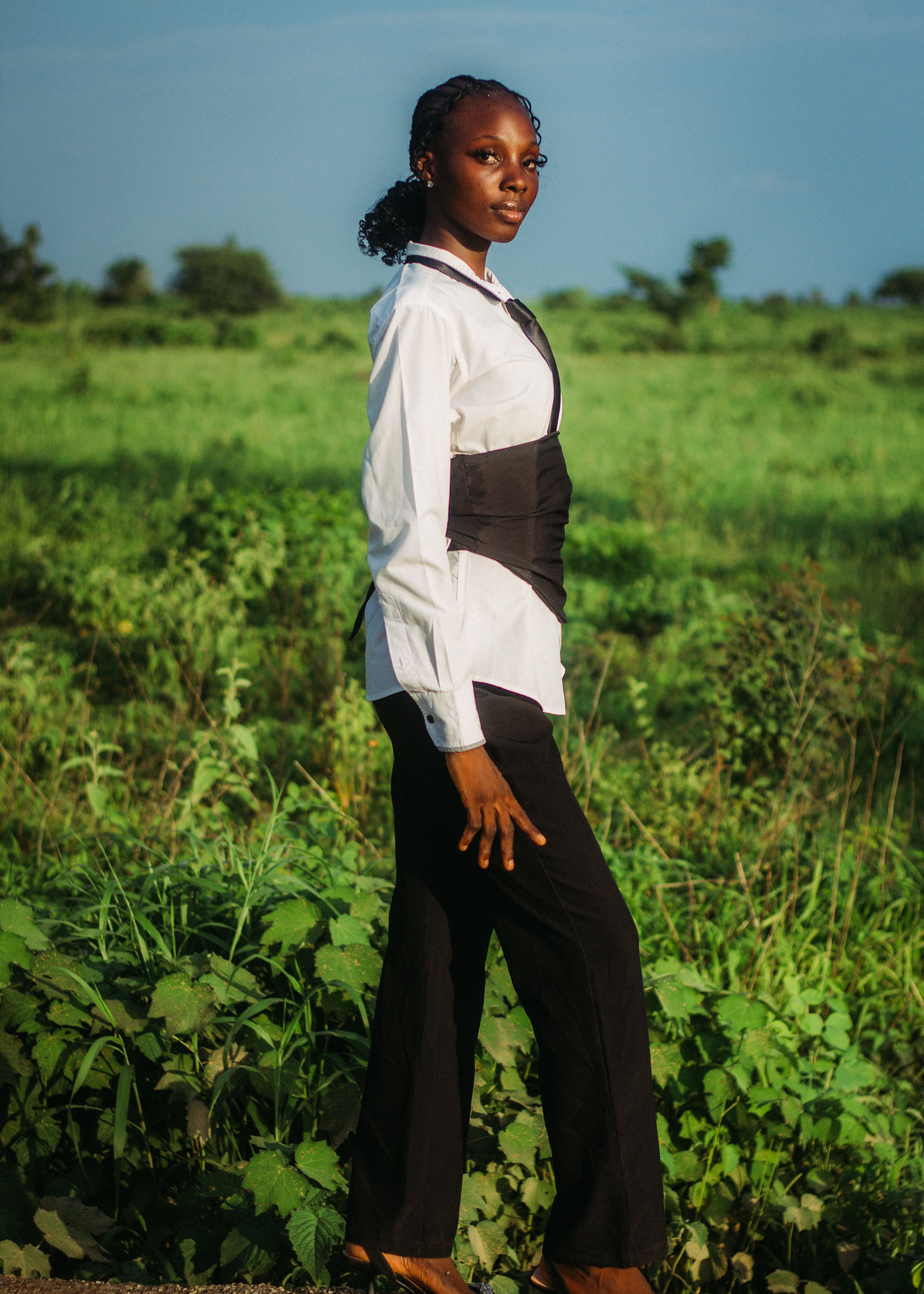 Stylish woman in formal attire posing confidently in a lush green field, embodying elegance and poise.