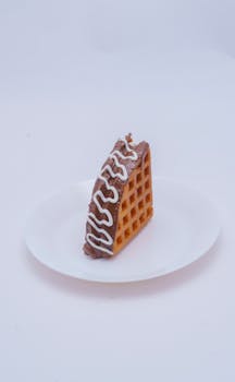 Close-up of a chocolate-covered waffle with white icing drizzle on a white plate.