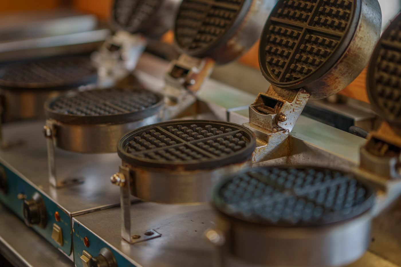 Several metal waffle makers with deep grid plates in a kitchen