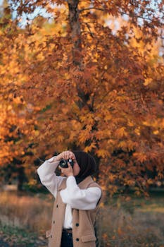 Woman photographing under vibrant autumn leaves in a park setting.