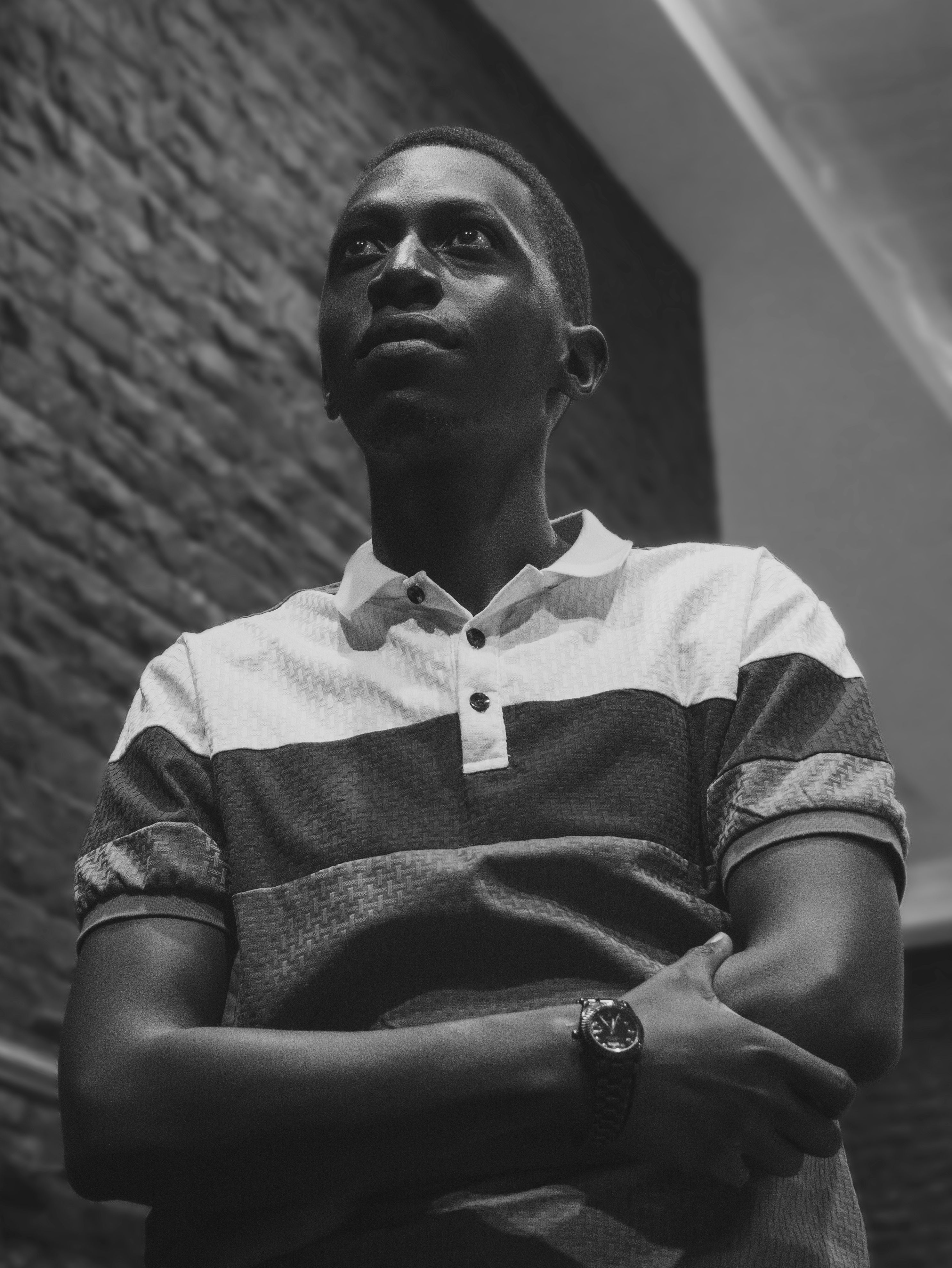 Black and white photo of a man in a reflective pose indoors with brick wall.