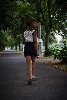 A young woman walks on a tree-lined pathway in a Berlin park during daytime.