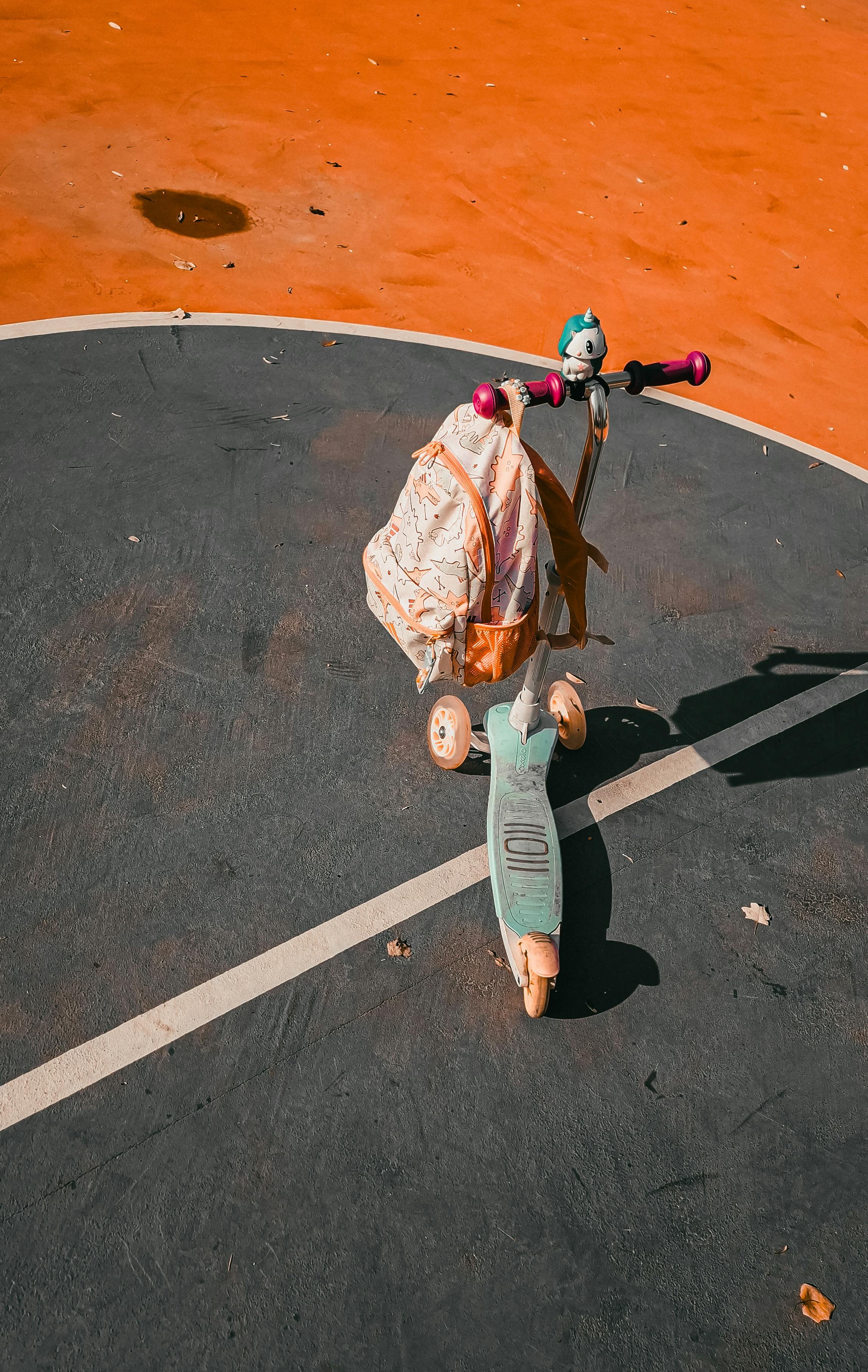 A child's scooter with a pink backpack on a colorful outdoor playground.