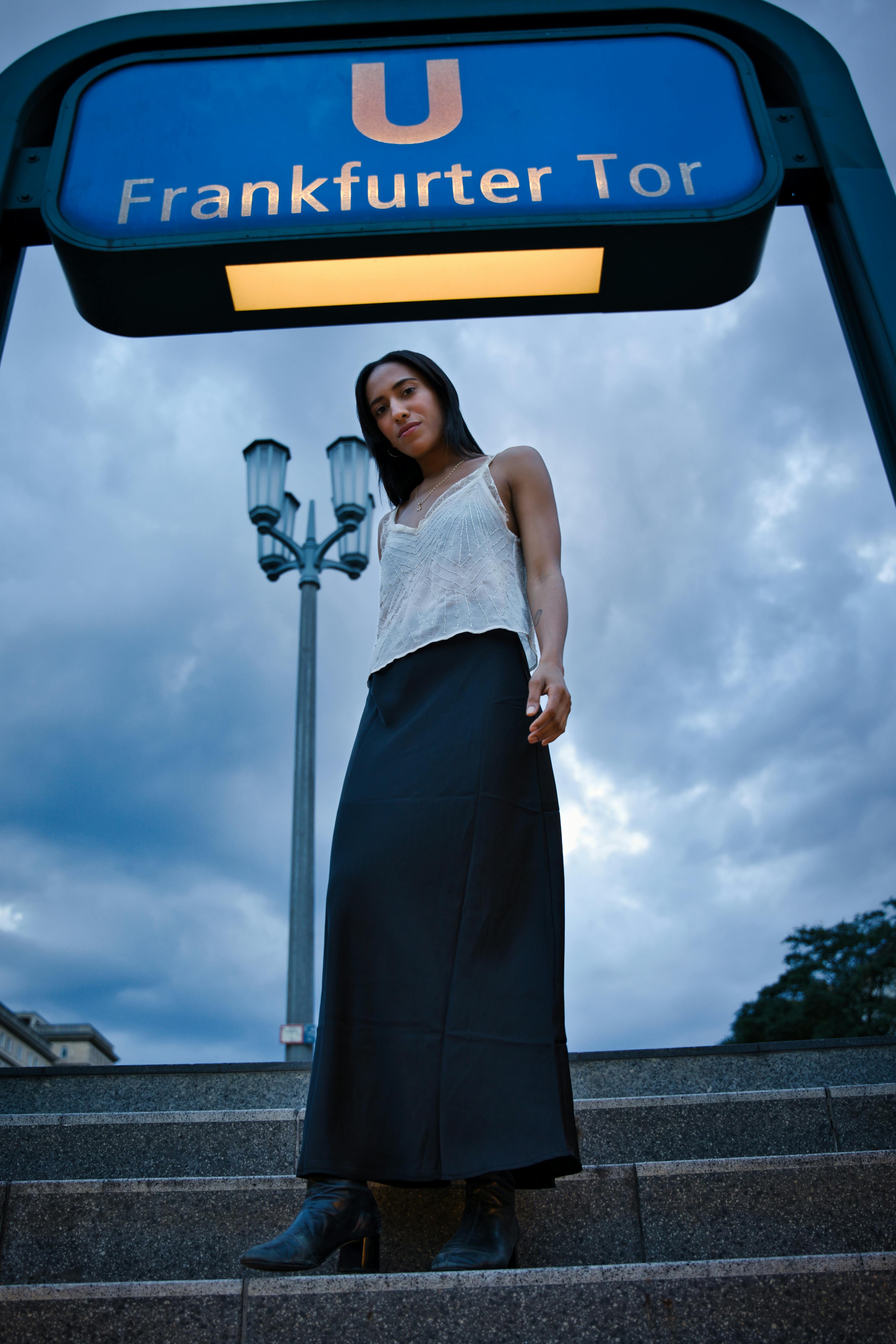 A stylish woman poses under the Frankfurter Tor sign in Berlin, Germany at twilight.