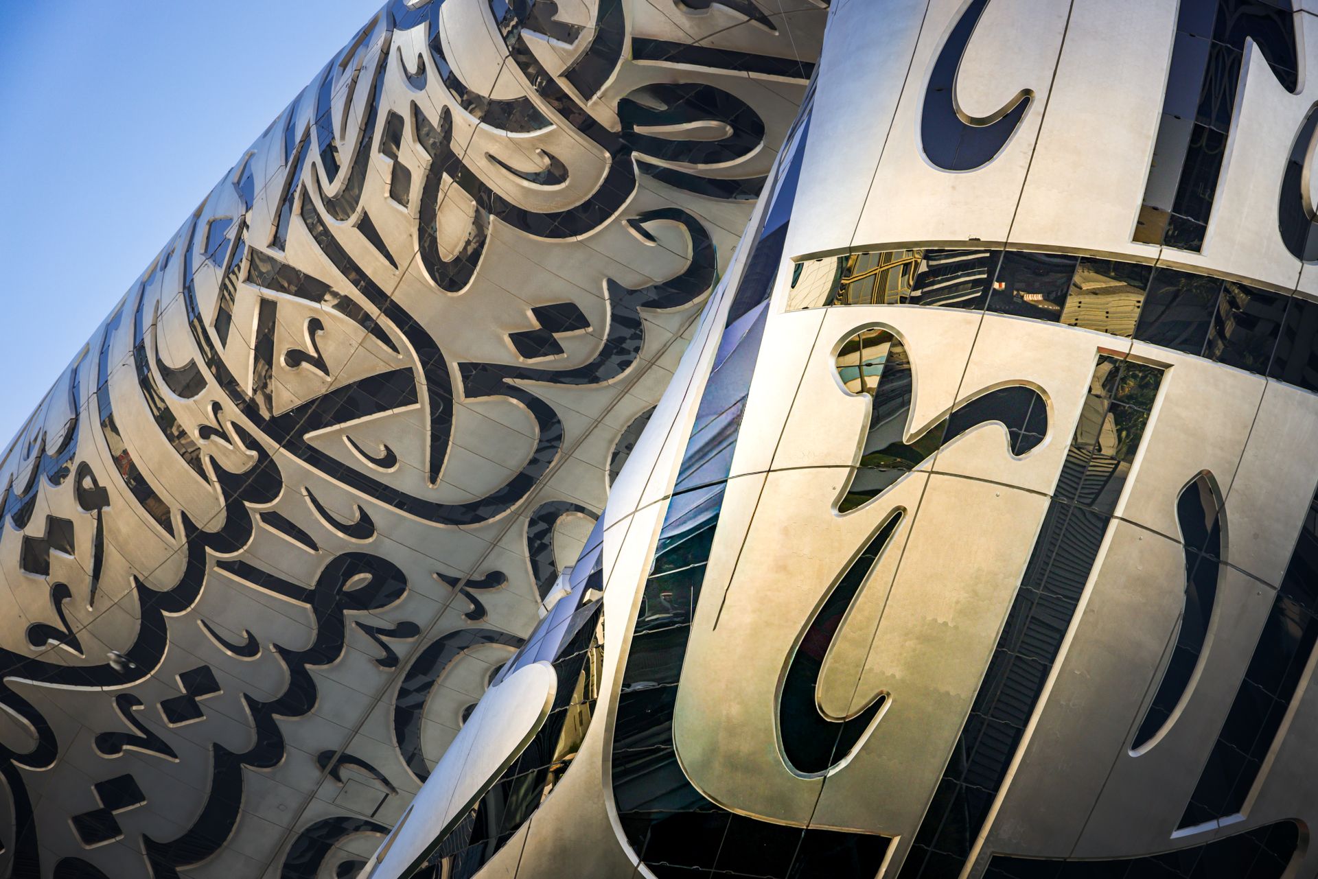Close-up of a futuristic building adorned with ornate Arabic calligraphy in a modern city setting.