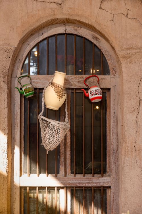 Free Old stone window adorned with colorful teapots and a woven water jug, bathed in sunlight. Stock Photo