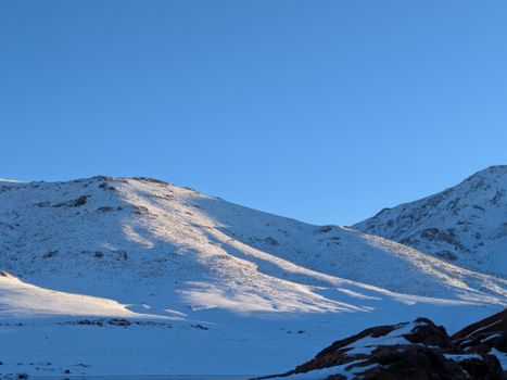 A tranquil scene of snow-covered mountains under a clear blue sky captured during daylight.
