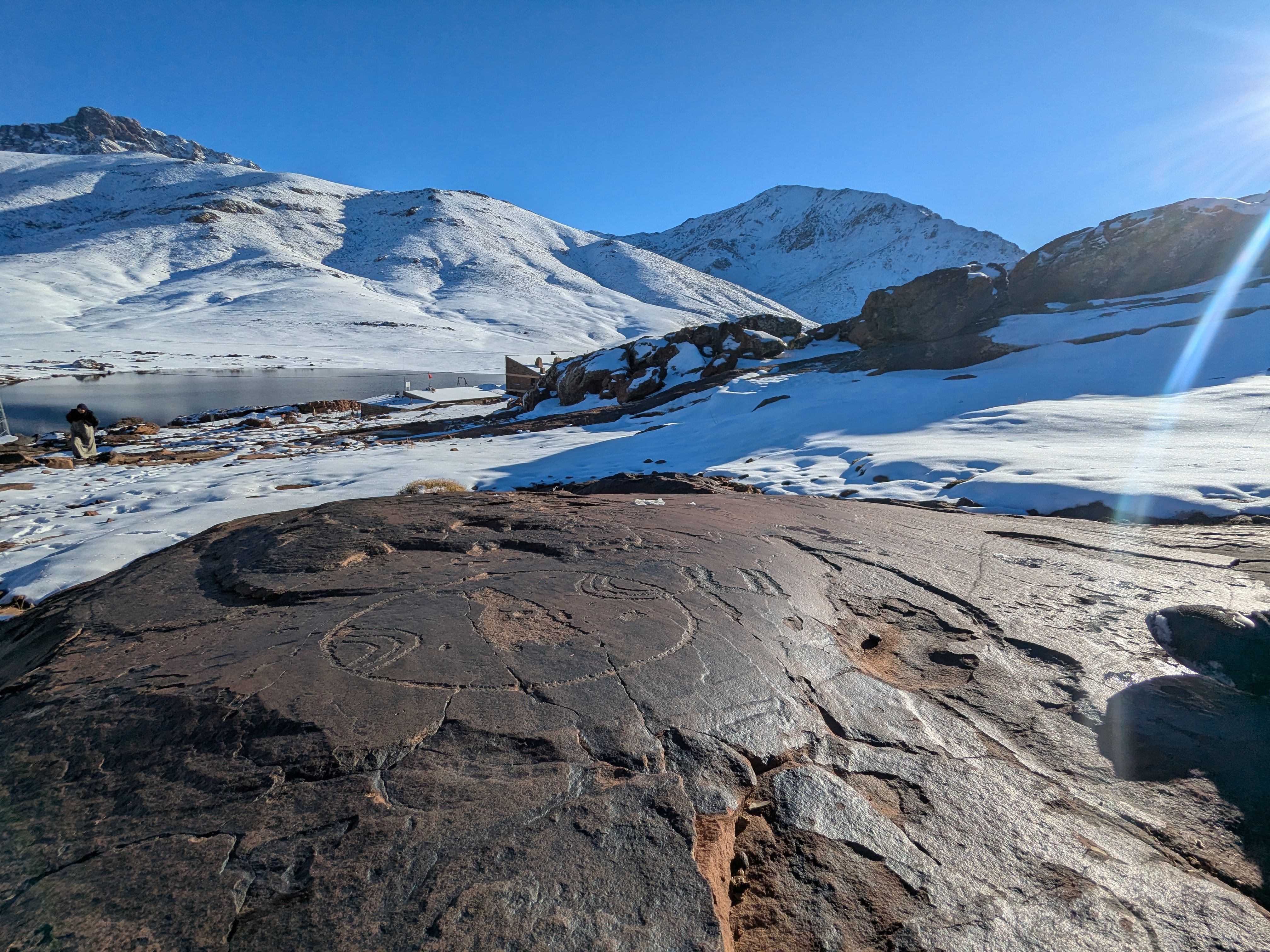 Scenic view of snow-covered mountains with ancient petroglyphs on rocks under a clear blue sky.