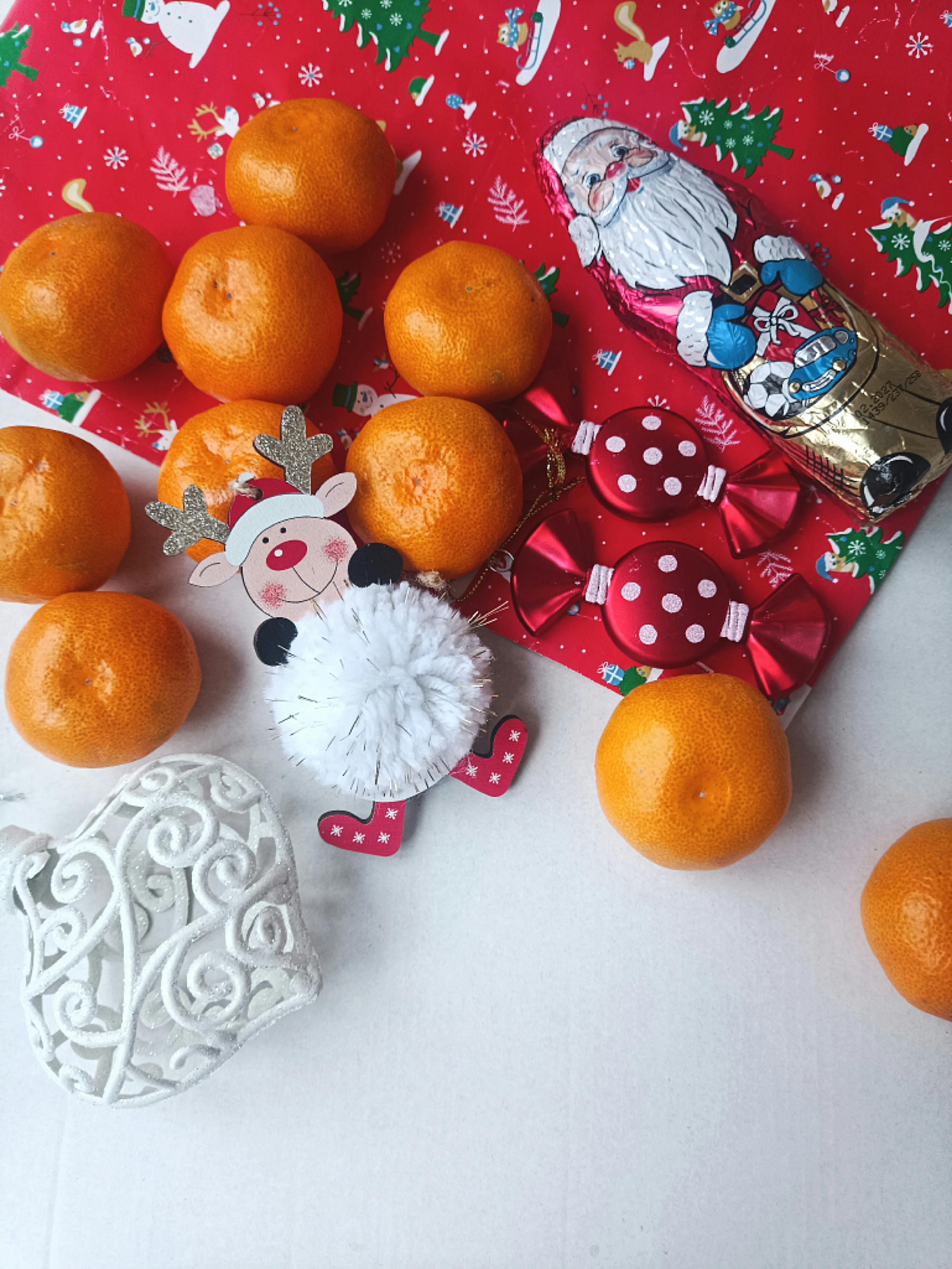 Flat lay of Christmas oranges, decorations, and Santa chocolate on a festive background.