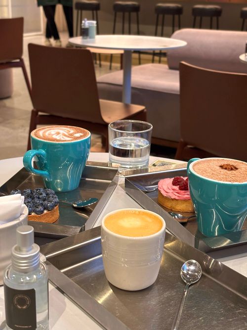Free Cozy cafe setting featuring cappuccino, latte, and desserts on modern trays, perfect for a relaxing break. Stock Photo