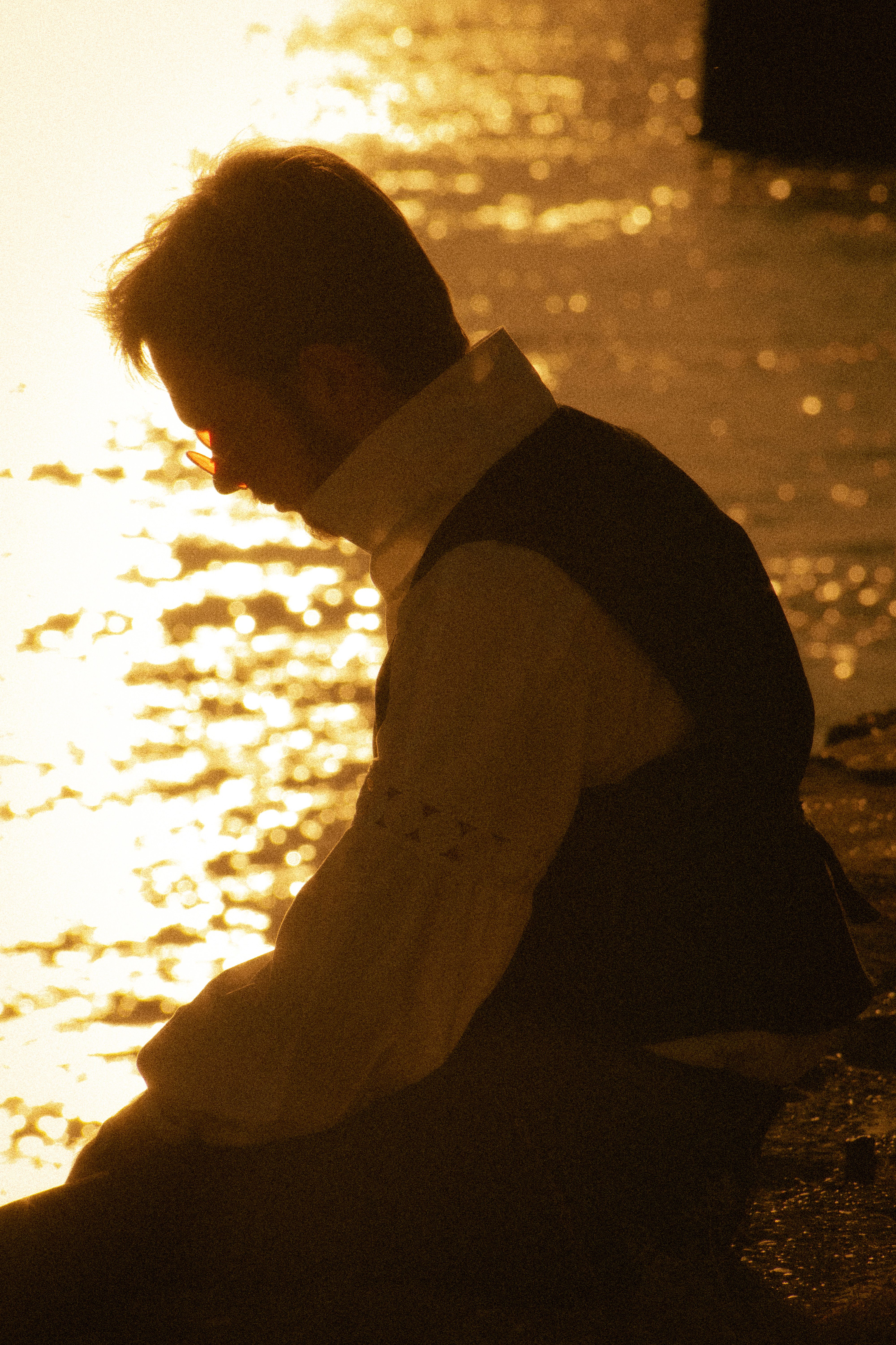 A man sits by the water's edge, his silhouette framed by a golden sunset.
