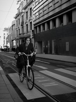 A woman rides a bicycle on an urban street with tram tracks. Black and white photo.