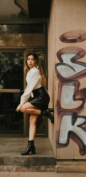 A stylish woman poses against a graffiti-covered wall, showcasing urban fashion.
