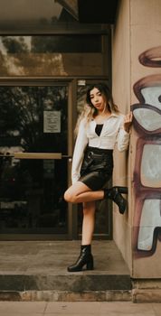Fashionable woman in chic outfit poses confidently against a city wall.