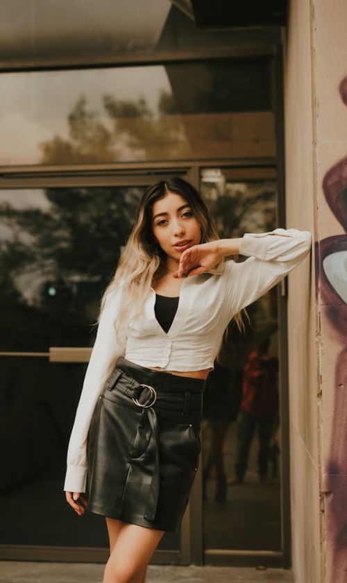 Free Young woman in trendy outfit poses confidently in urban setting against a glass background. Stock Photo