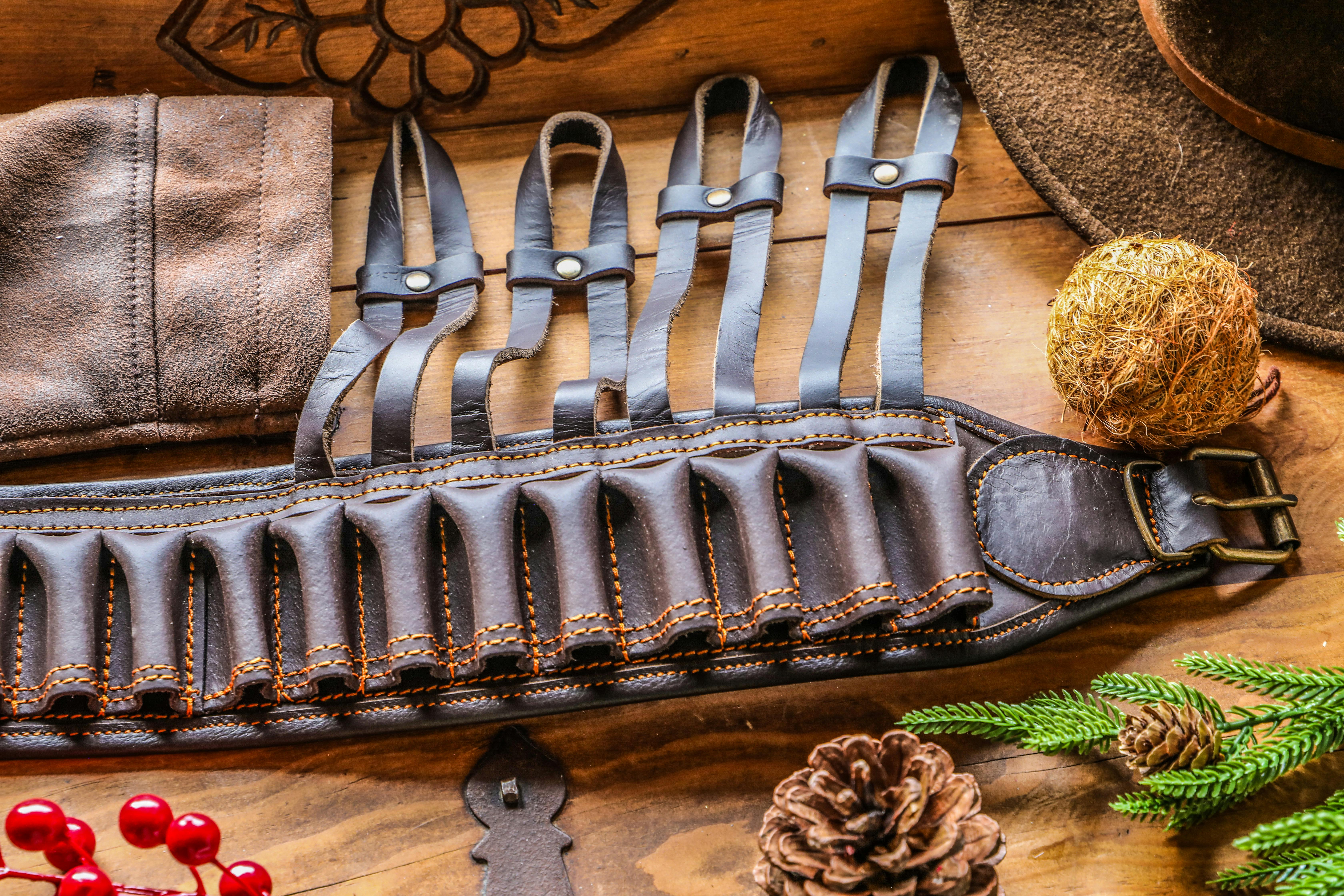 Leather ammo belt with cowboy gear, pine cones, and rustic decor on wooden table.