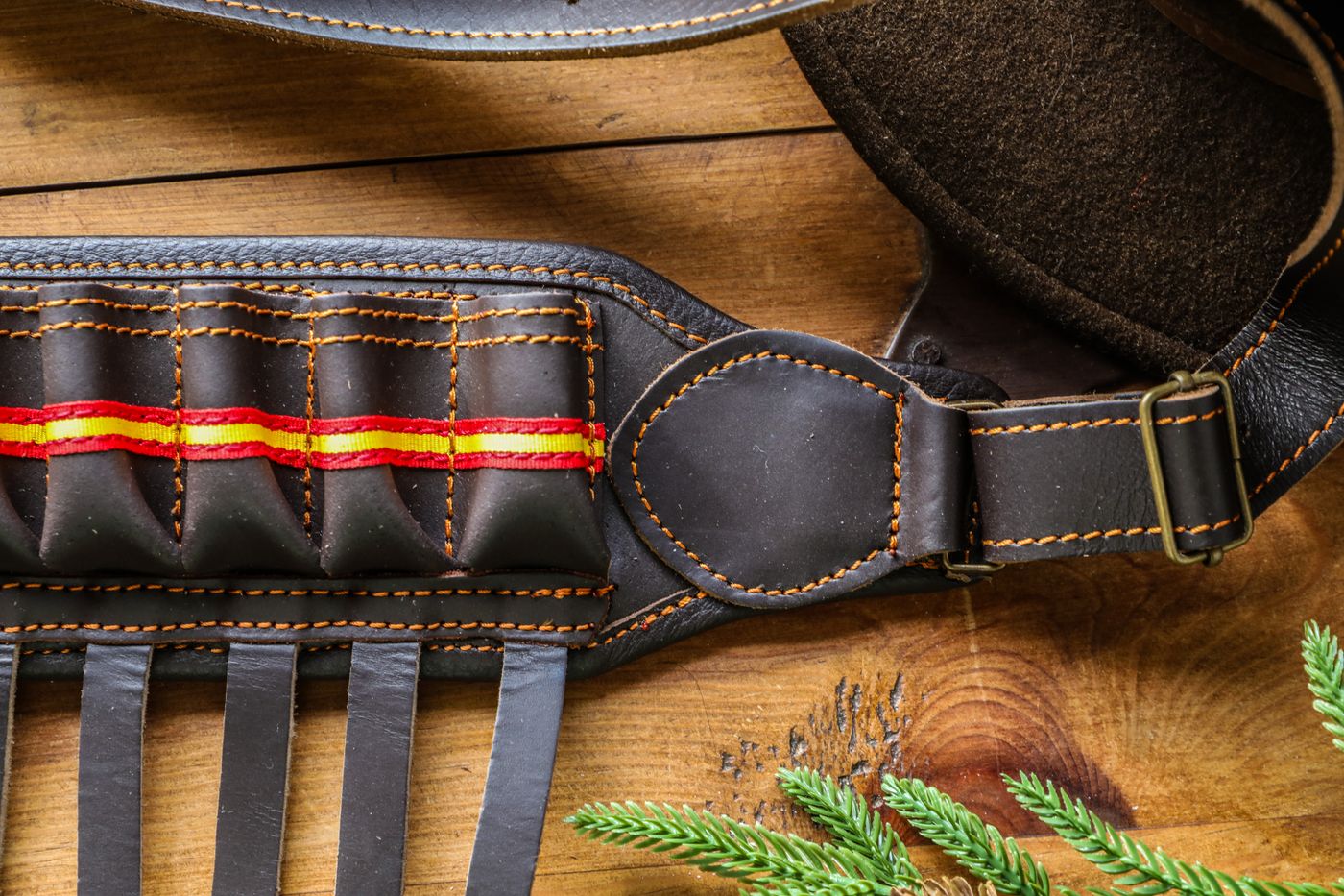 Detailed view of a leather rifle sling with cartridge holders and colorful stitching on a wooden background.