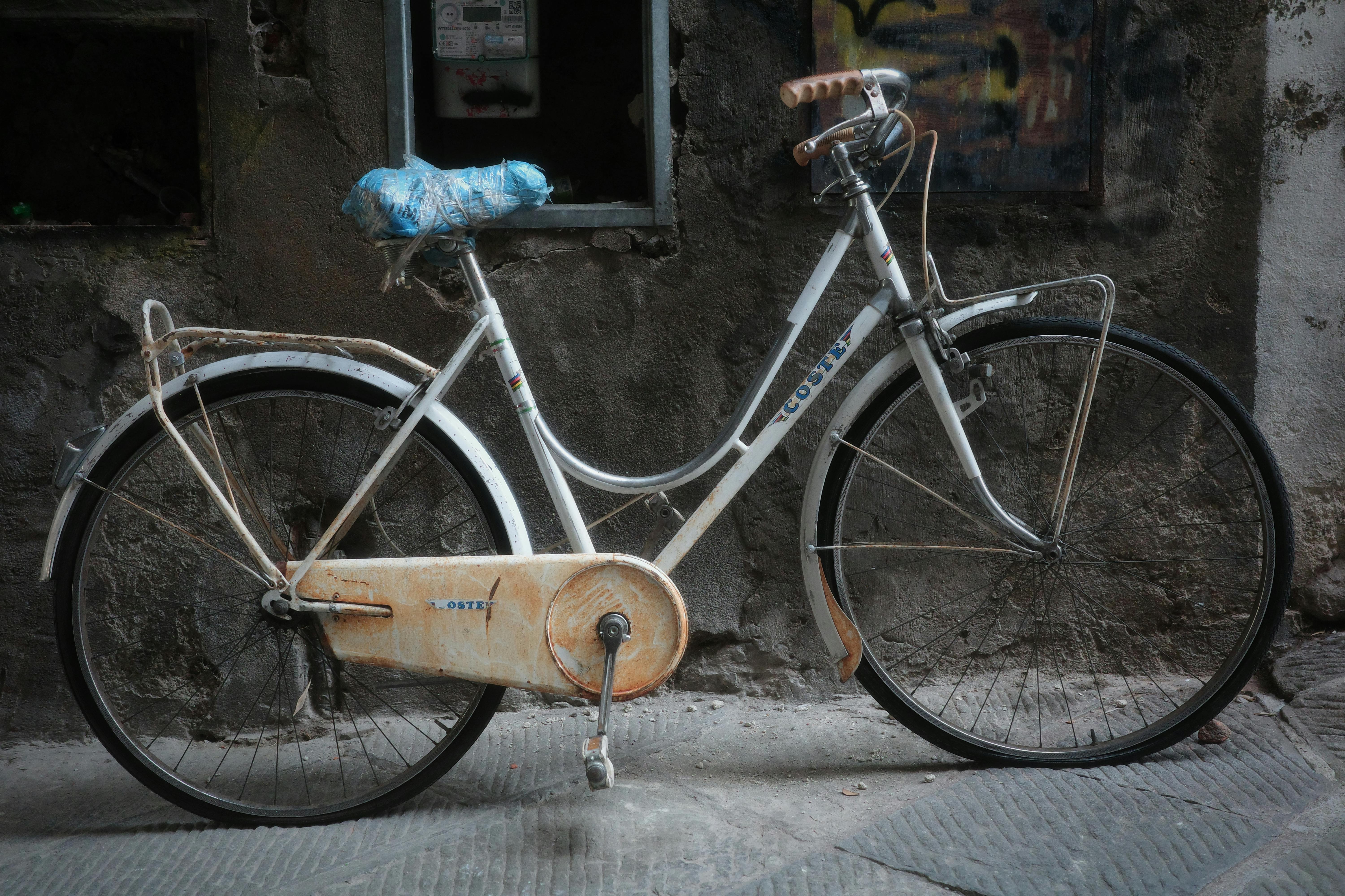 Aged white bicycle leaning against a weathered wall in an urban alleyway.