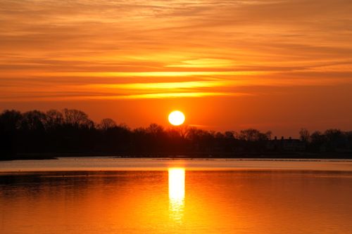Free Breathtaking sunset with vibrant orange hues reflecting over a serene lake. Stock Photo