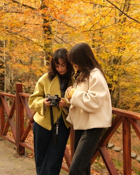 Two women review photos on a digital camera in a vibrant autumn forest.