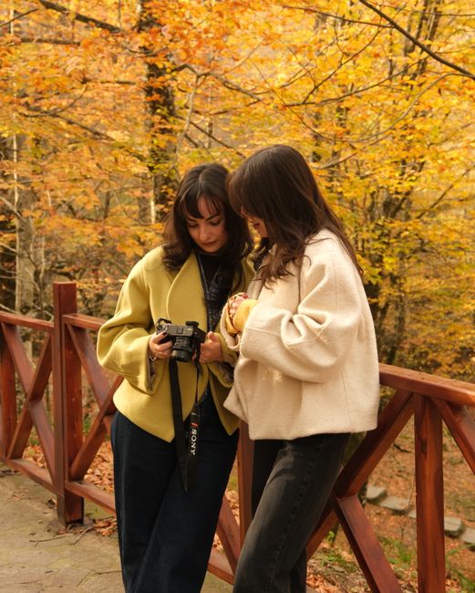 Two women review photos on a digital camera in a vibrant autumn forest.