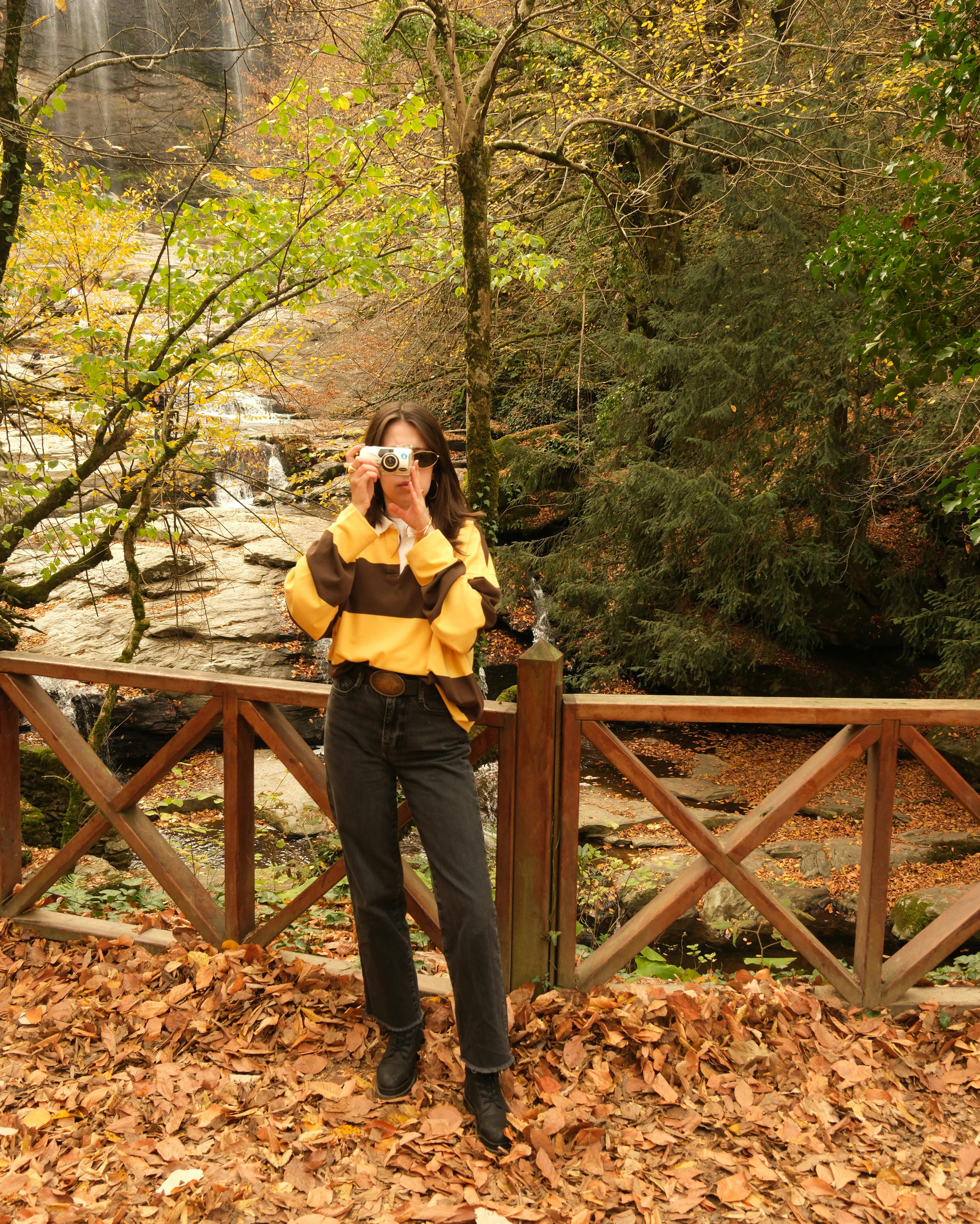 Woman captures autumn view with vintage camera by waterfall.