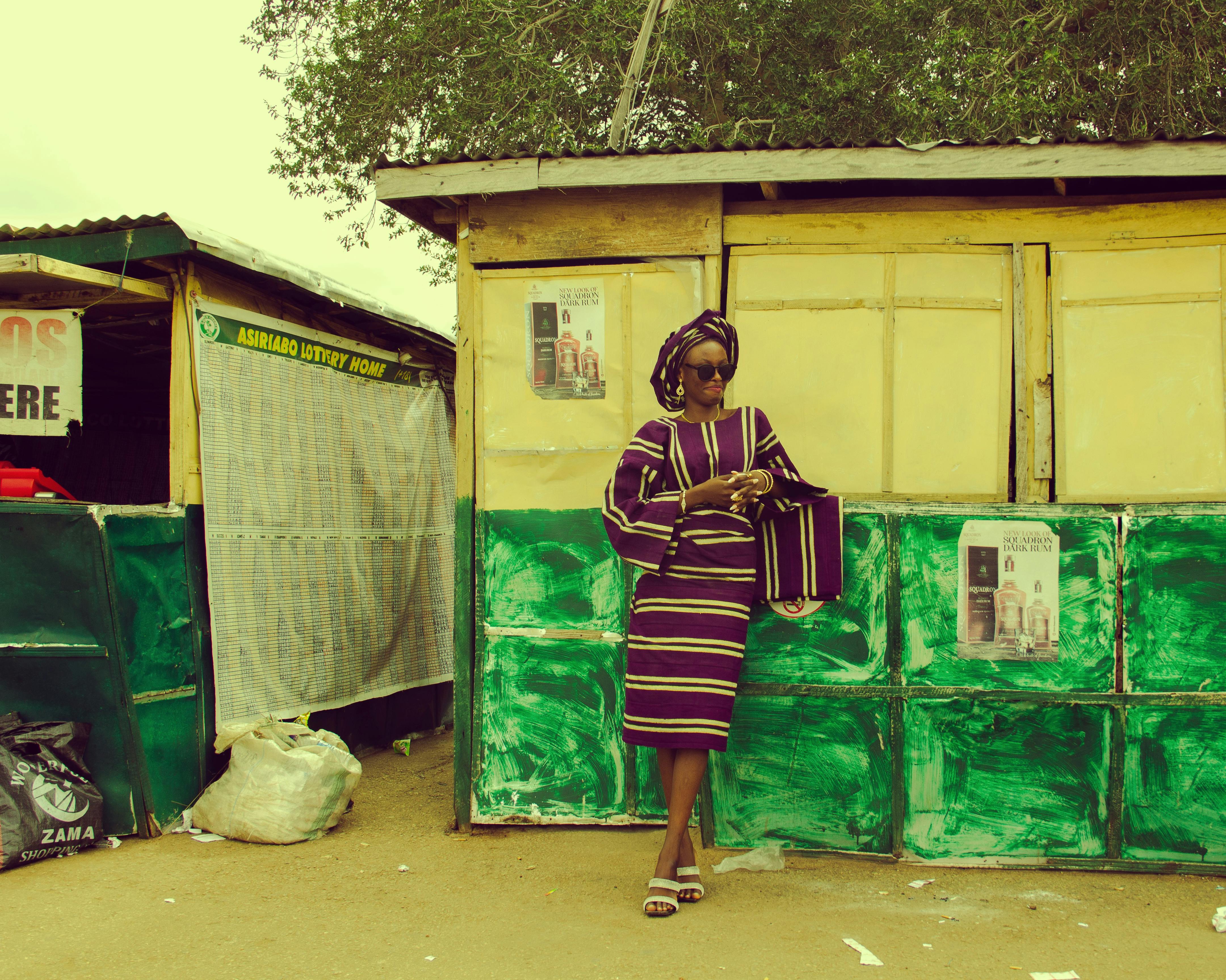 Stylish African woman in traditional attire standing by a vibrant shop outdoors.