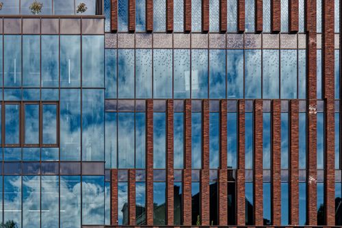 Free Abstract view of a modern building facade with glass reflecting a cloudy sky. Stock Photo