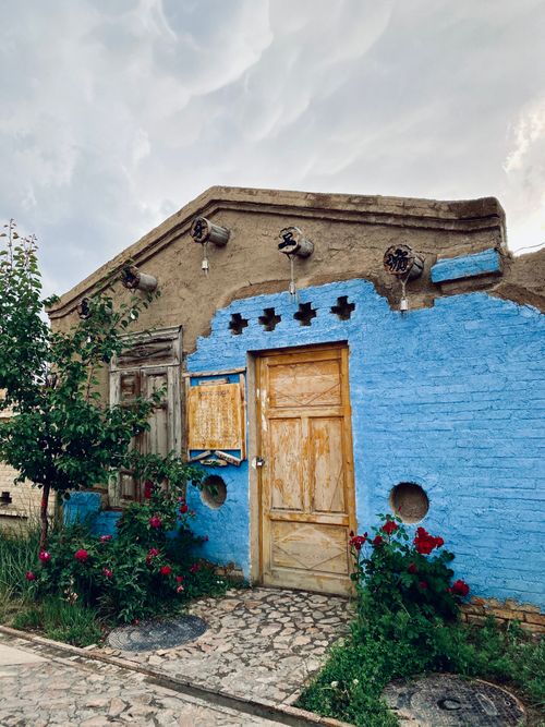 Free A vibrant blue and earthy brown traditional house in Xinjiang, with lush flowers and rustic architecture. Stock Photo