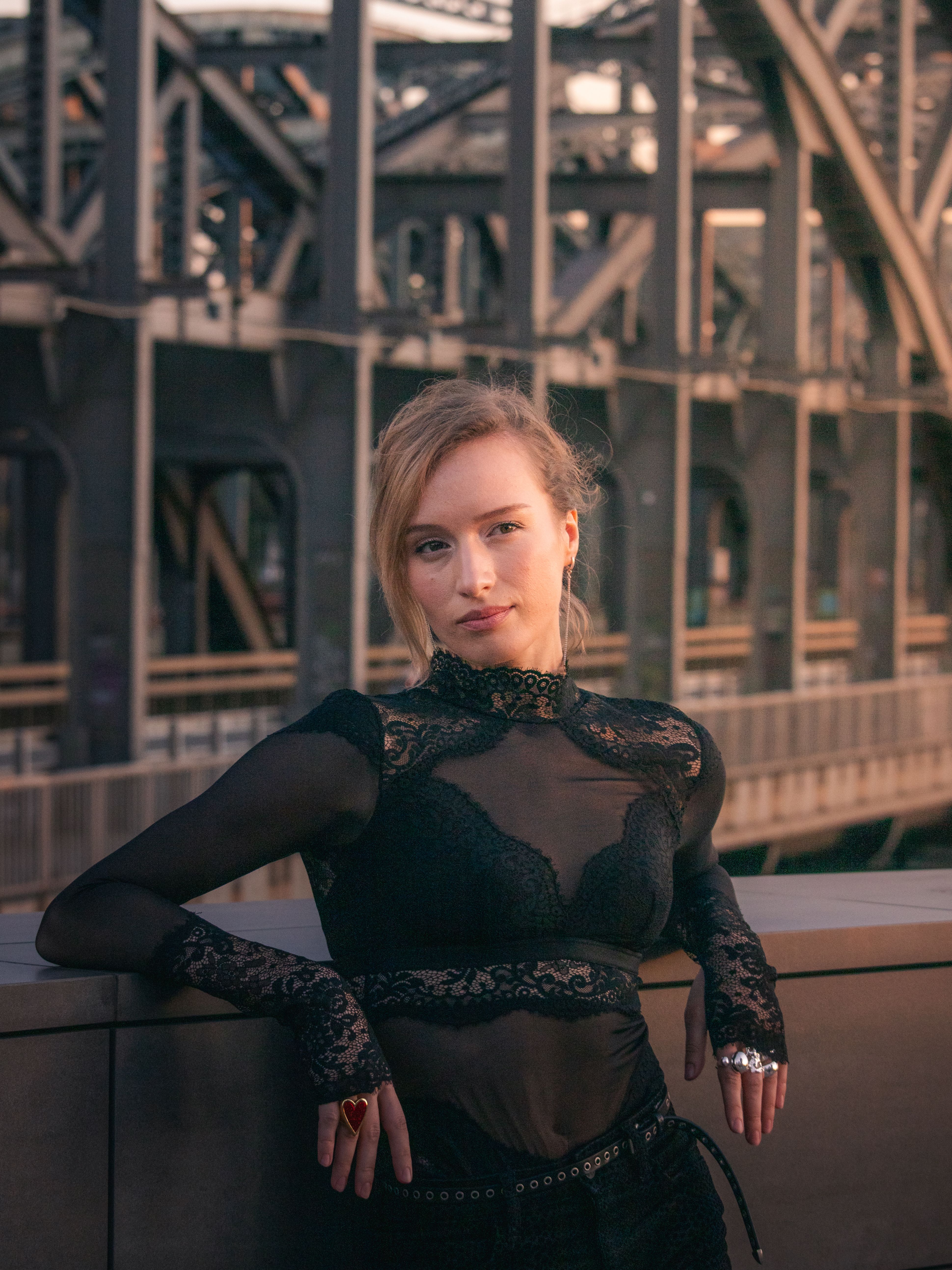 A stylish woman poses against a historic bridge in Hamburg, showcasing modern fashion.