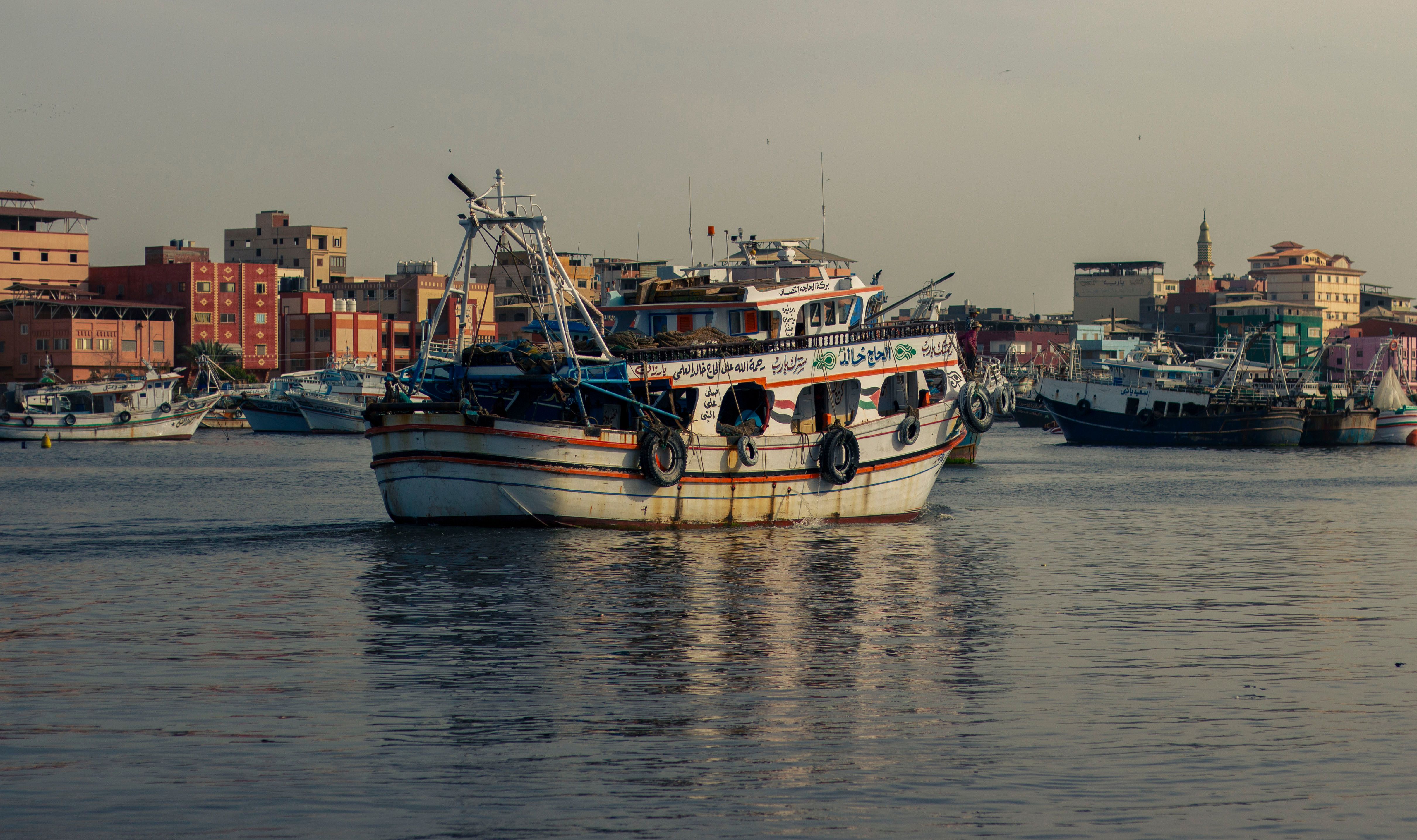 Fishing Boat Docked in Bustling Urban Harbor · Free Stock Photo