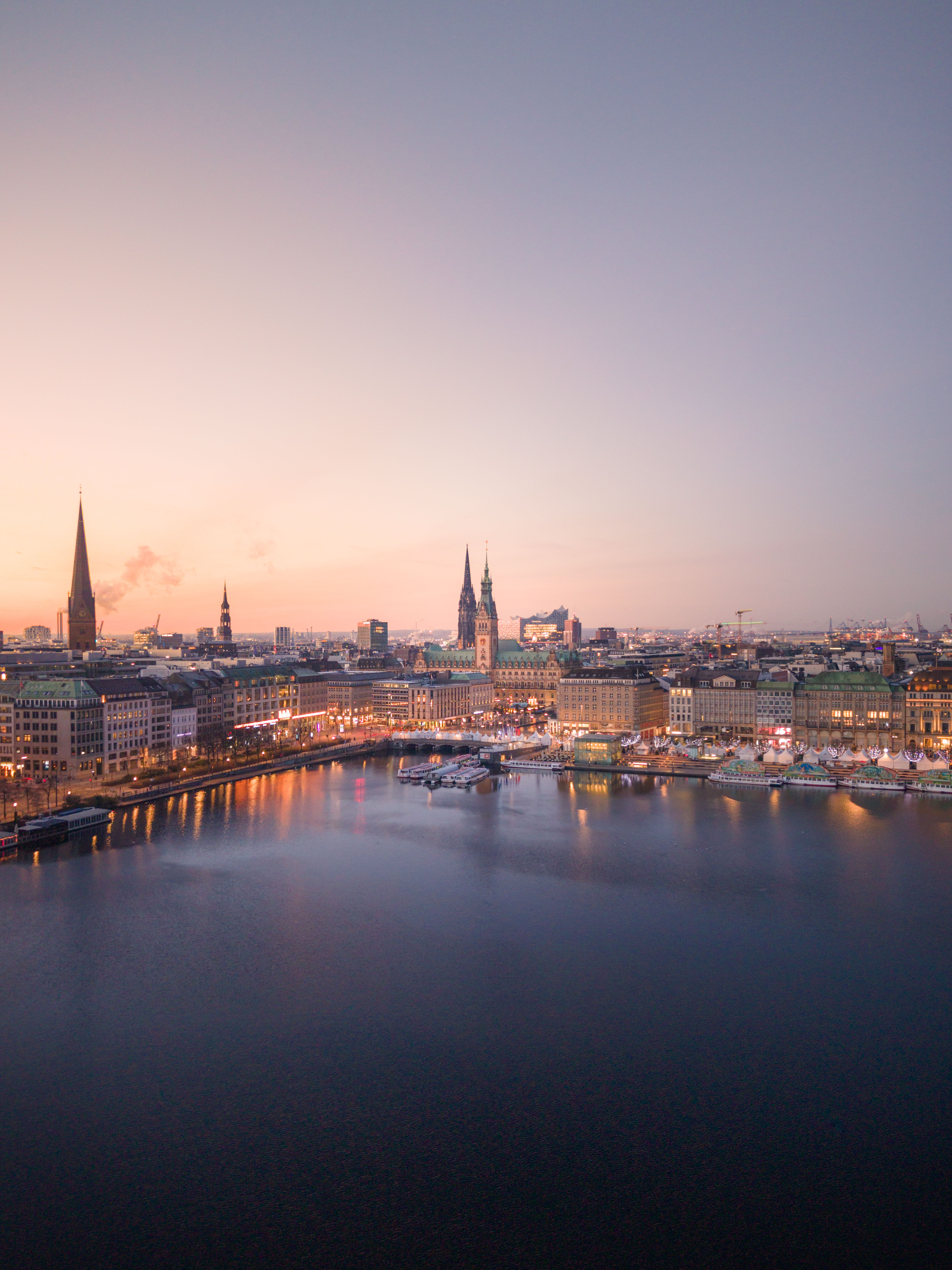 Stunning aerial view of Hamburg skyline with iconic landmarks at sunset, reflecting over the water.