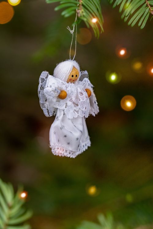 Free Close-up of a wooden angel Christmas ornament hanging on a tree branch with blurred lights. Stock Photo