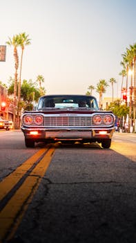 Front view of a vintage car on a palm-lined street at sunset, California vibe.