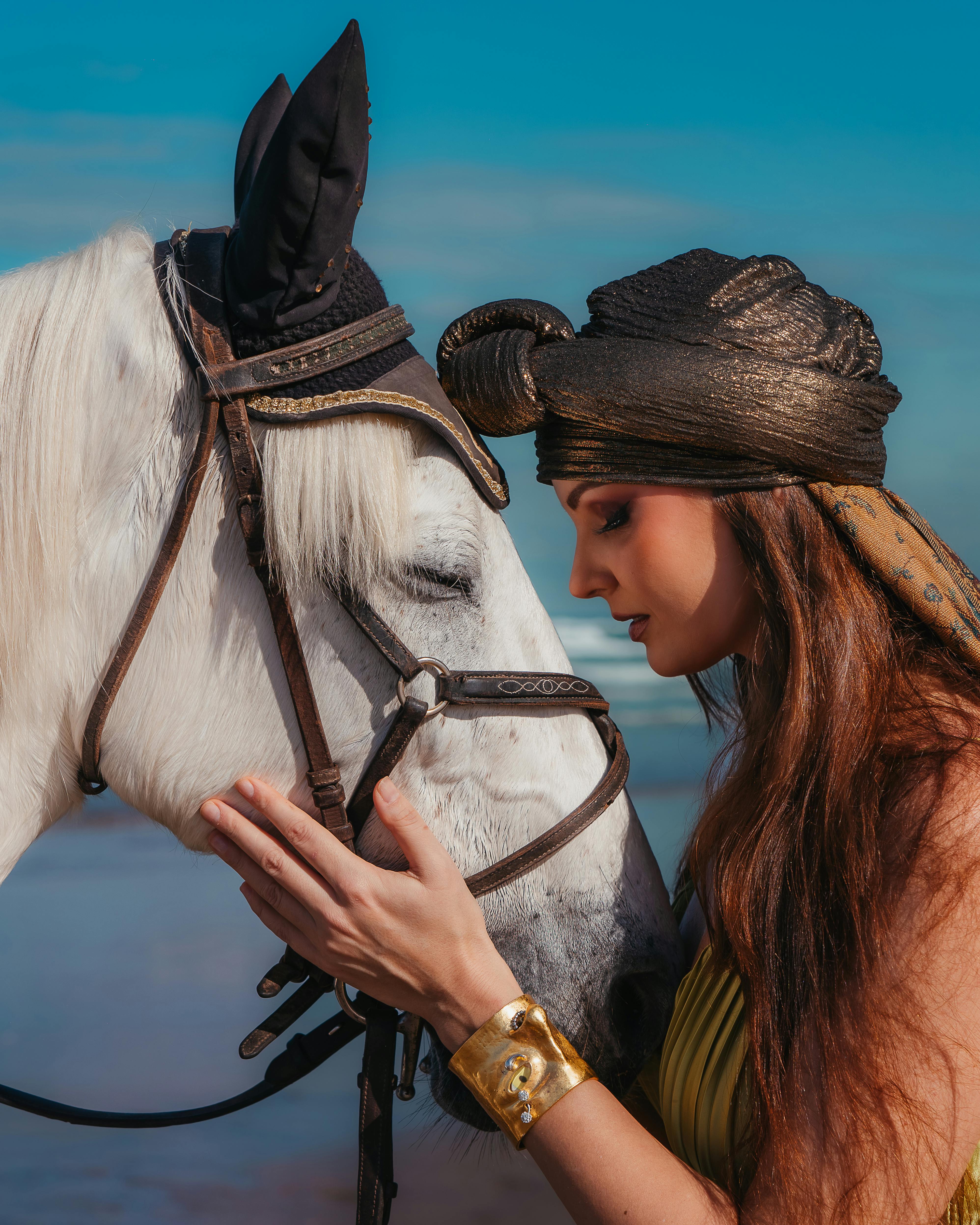 De franc Escena serena d'una dona amb turbant unint-se a un cavall blanc vora el mar. Foto d'estoc