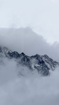 Snow-covered mountain peaks emerging through clouds, creating a dramatic and serene landscape.