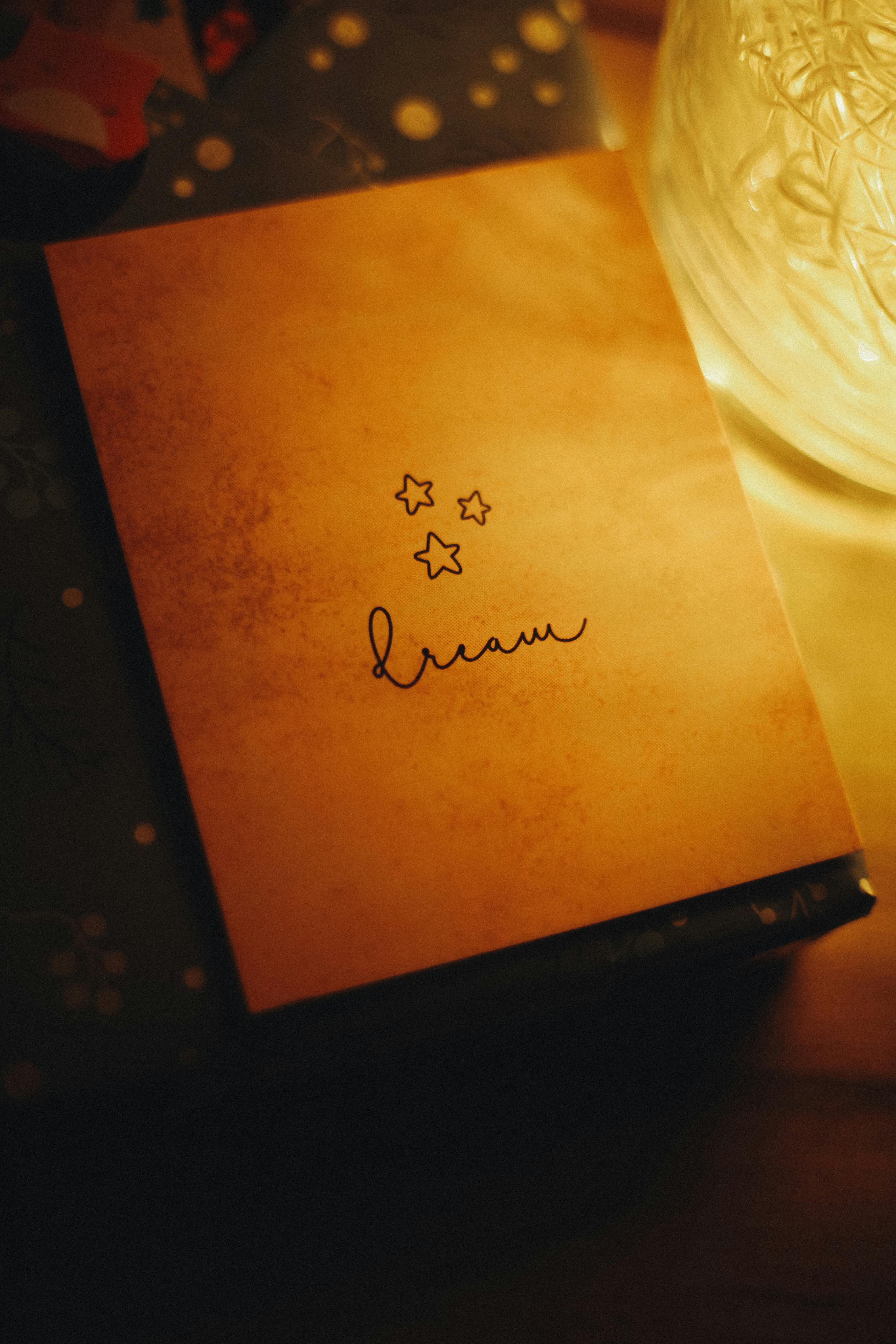 grátis Uma cena com iluminação quente, apresentando um caderno com a palavra "sonho" escrita nele, evocando relaxamento e inspiração. Foto profissional