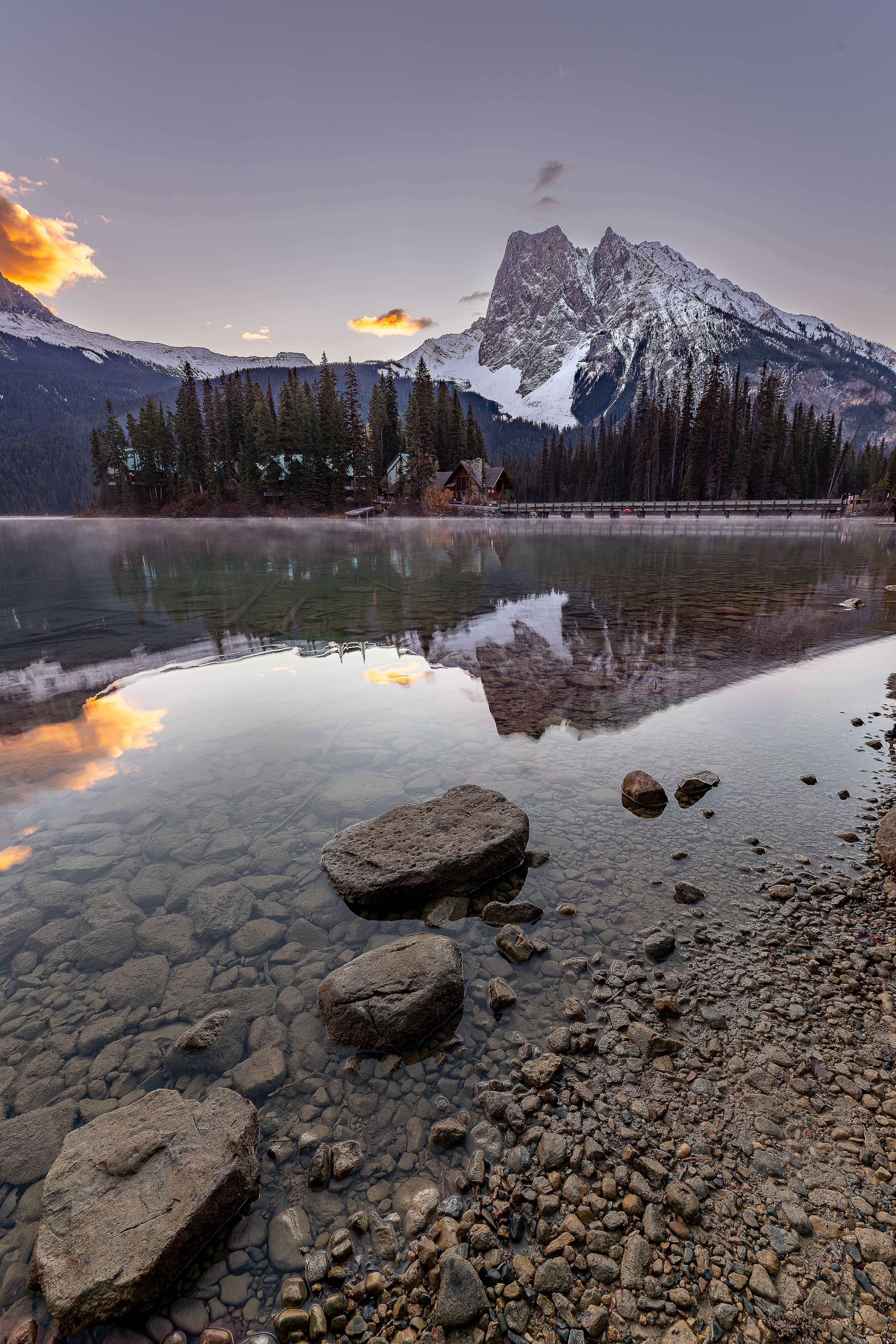 Breathtaking sunset view over a tranquil lake with a snow-capped mountain reflection.