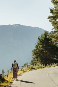 A lone hiker with a backpack walks along a winding mountain road under a clear sky.