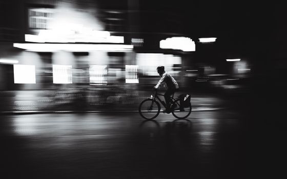Black and white photo of a cyclist moving quickly through Berlin streets at night.