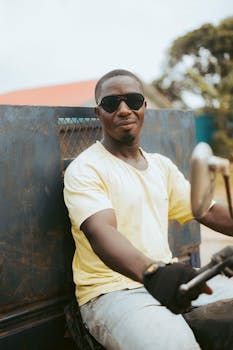 Smiling man in sunglasses riding a motorcycle outdoors on a sunny day.