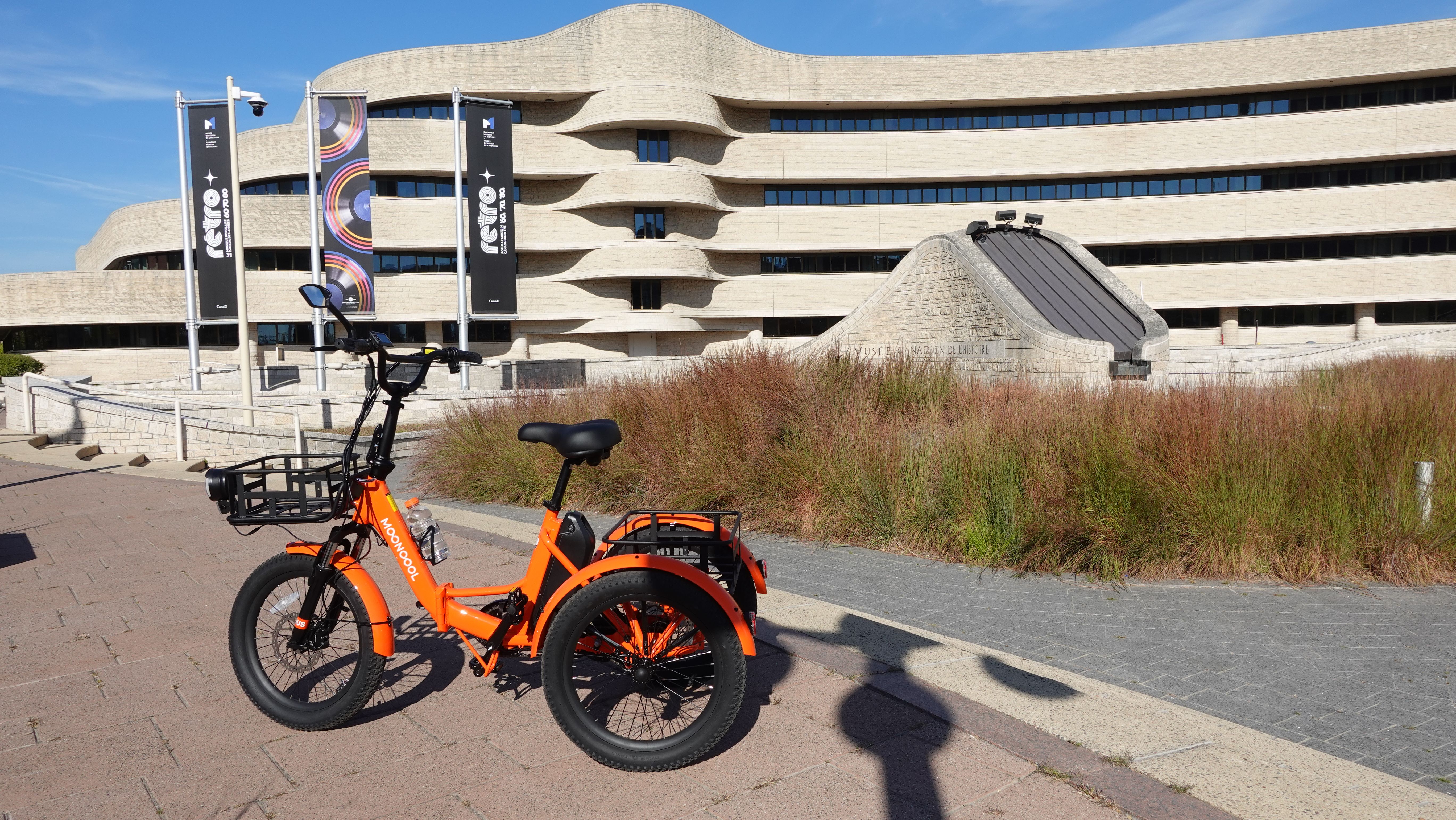 Bright orange electric bike parked in front of contemporary wavy building facade.