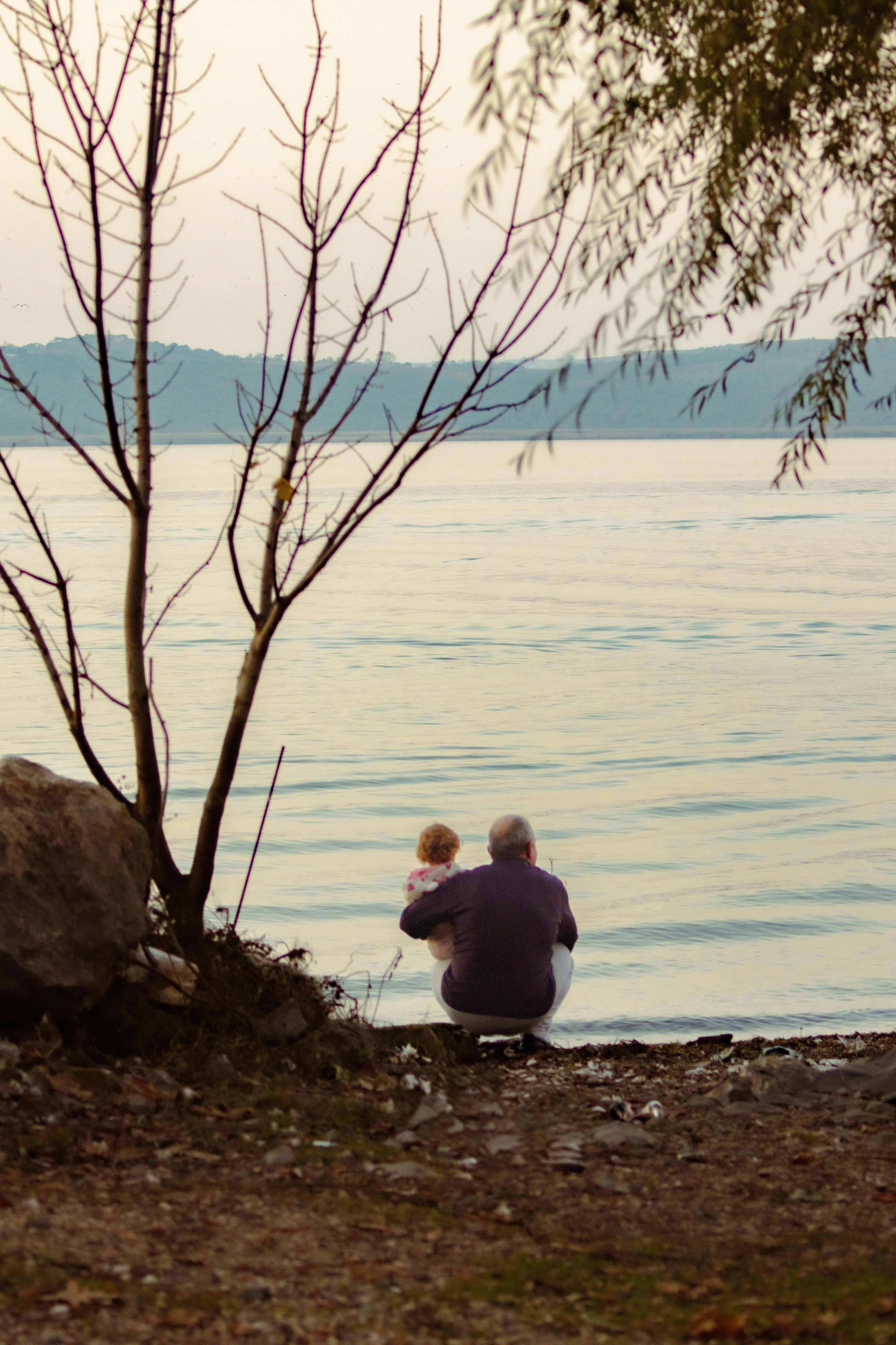 Grandparent and child by a tranquil lake in Bursa, Türkiye at sunset.